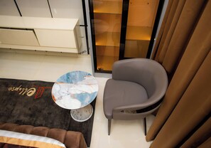 A small room with a sofa, a chair, a coffee table, and a sliding glass door. - Ellipse Hotels (Lagos)