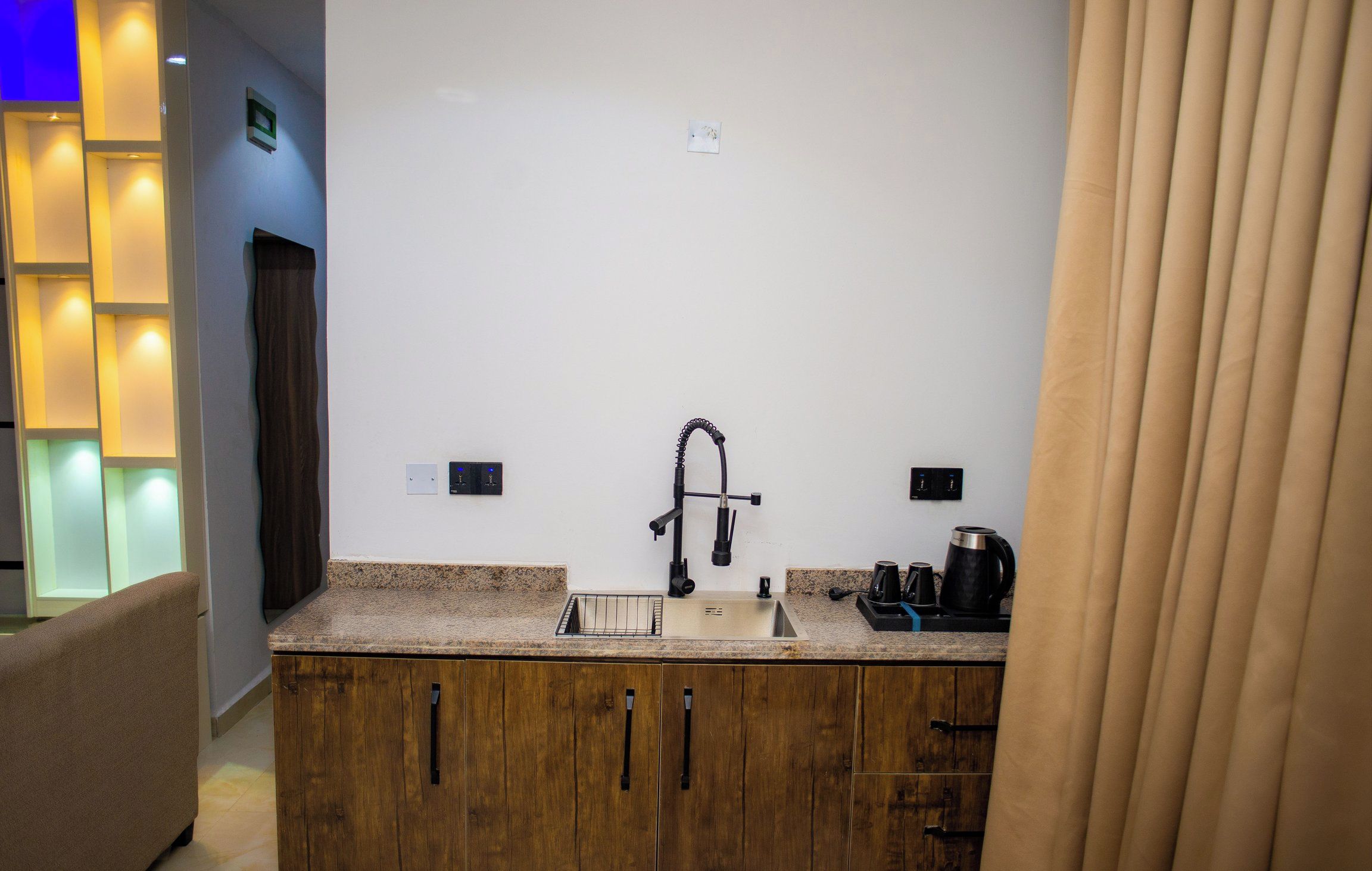 Una cocina moderna con encimera de granito, armarios de madera, pileta de acero inoxidable y cafetera.