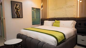 A modern bedroom with a large bed, bedside tables, a round side table, and a wall-mounted artwork.