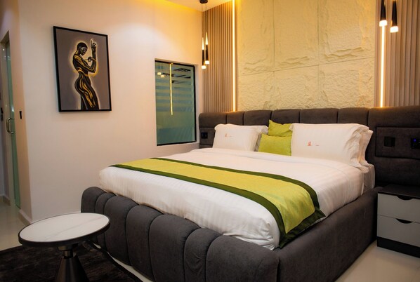 A modern bedroom with a large bed, bedside tables, a round side table, and a wall-mounted artwork. - Ellipse Hotels (Lagos)
