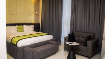 Una camera d'hotel con un letto grande, un divano grigio, un tavolino rotondo e una finestra con tende.