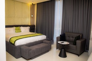 A hotel room with a large bed, a grey sofa, a small round table, and a window with curtains.
