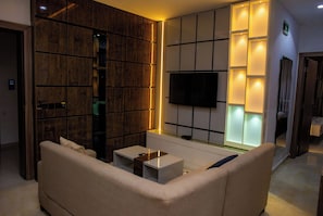 A modern living room with a sofa, a coffee table, and a flat-screen TV mounted on the wall. - Ellipse Hotels (Lagos)