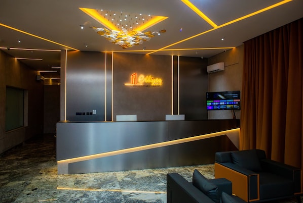 A hotel reception area with a modern design, including a reception desk, a digital screen, and a chandelier. - Ellipse Hotels (Lagos)