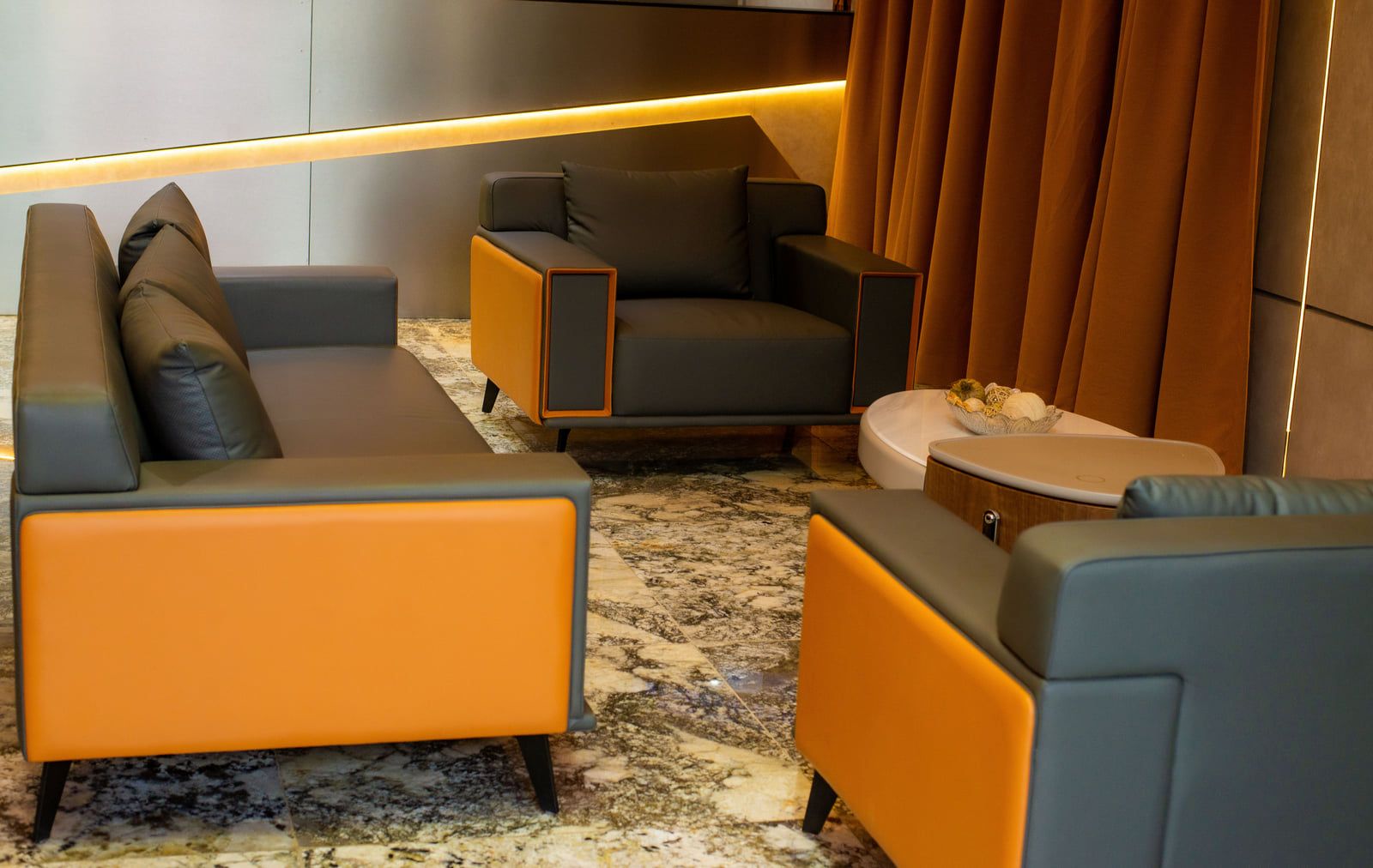 Una sala de estar moderna con un sofá, un sillón y un reposapiés, un piso de mármol y una lámpara de pared.
