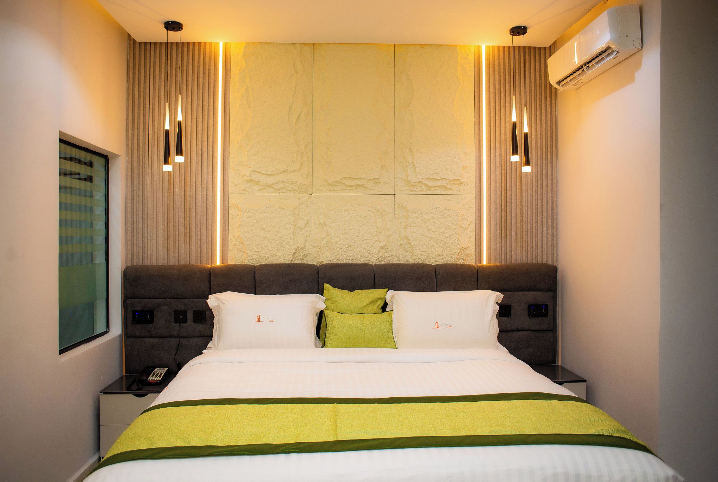 Habitación de hotel con una cama grande, controles junto a la cama, un teléfono y un equipo de aire acondicionado.