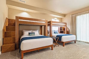 A hotel room with two bunk beds, a wooden headboard, a small table, and a window with curtains. - Granite View Prescott Cabin - Hot Tub & Game Room Near Whiskey Row (Prescott)