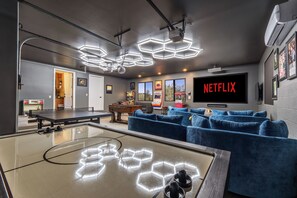 Un salon moderne avec une table de ping-pong, des canapés bleus et un grand écran de télévision affichant le logo « NETFLIX ».
