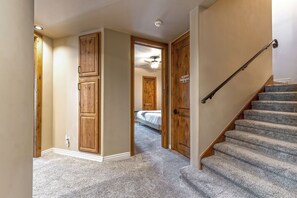 Un couloir avec des portes en bois, un escalier recouvert de moquette et un ventilateur de plafond.