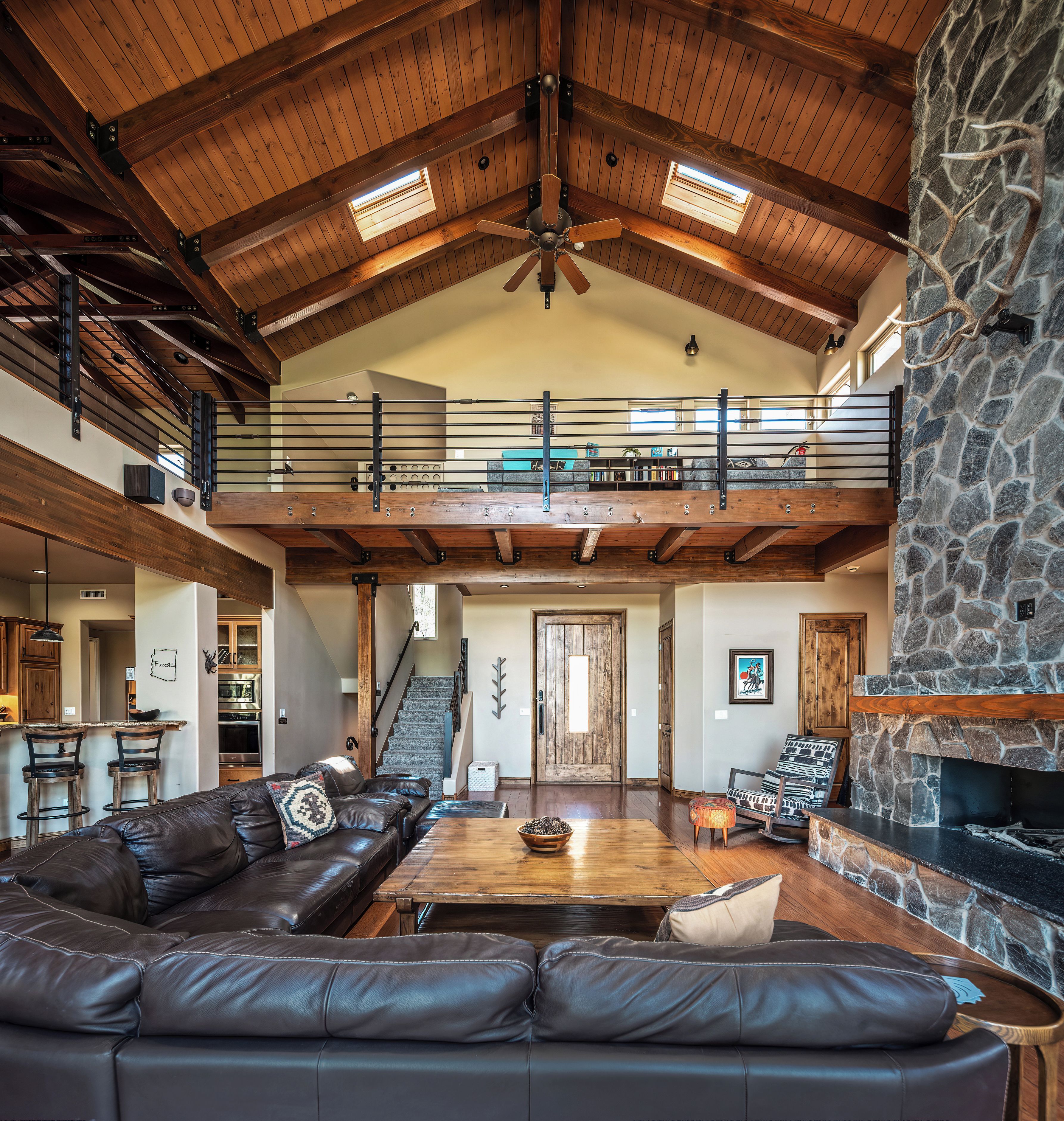 A spacious living area with a stone fireplace, leather seating, and a mezzanine level with a balcony.