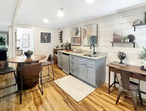 A modern kitchen with a central island, a dining area with chairs, and a kitchen island with a sink. - Doe Run Hideaway - Pet Friendly | Hot Tub | Game Room | Firepit (Ellijay)