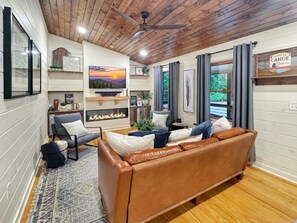 A cozy living room with a fireplace, leather sofa, and a television mounted on the wall. - Doe Run Hideaway - Pet Friendly | Hot Tub | Game Room | Firepit (Ellijay)