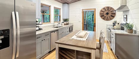 A modern kitchen with stainless steel appliances, wooden flooring, and a dining area with a wooden table.