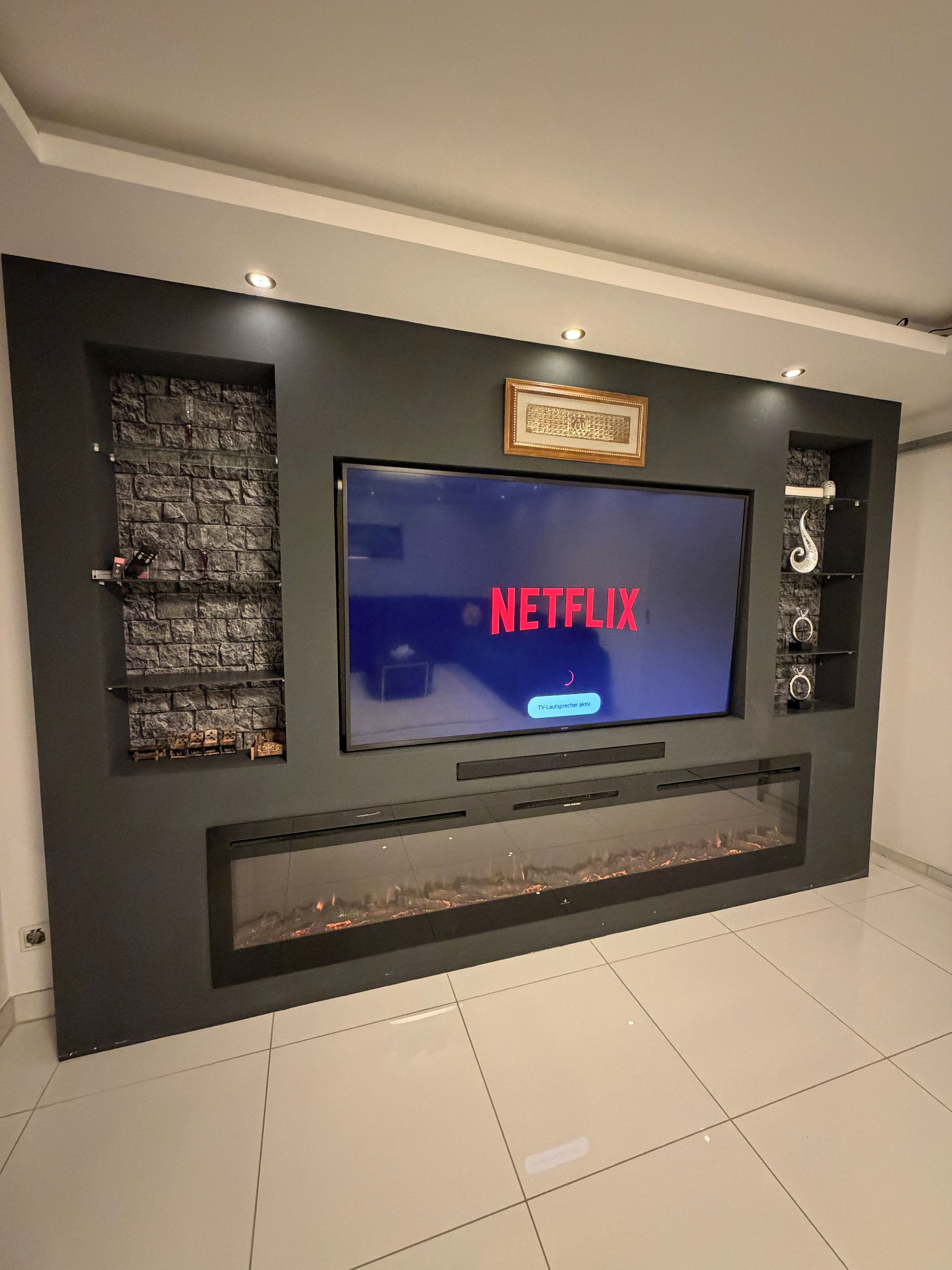Eine moderne Unterhaltungswand mit einem Flachbildfernseher, der 'NETFLIX' anzeigt, und einem Kamin darunter.