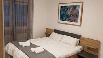 A modern bedroom with a bed, bedside tables, a window with curtains, and a framed abstract painting on the wall.