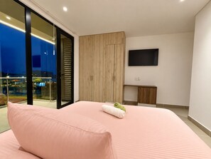 A modern bedroom with a large bed, a TV mounted on the wall, and a sliding glass door leading to an outdoor area. - Hotel Boutique Manacal (Inírida)