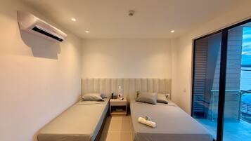 Habitación de hotel moderna con dos camas individuales, aire acondicionado integrado, mesita de noche con teléfono y lámpara, y un amplio ventanal con vistas.