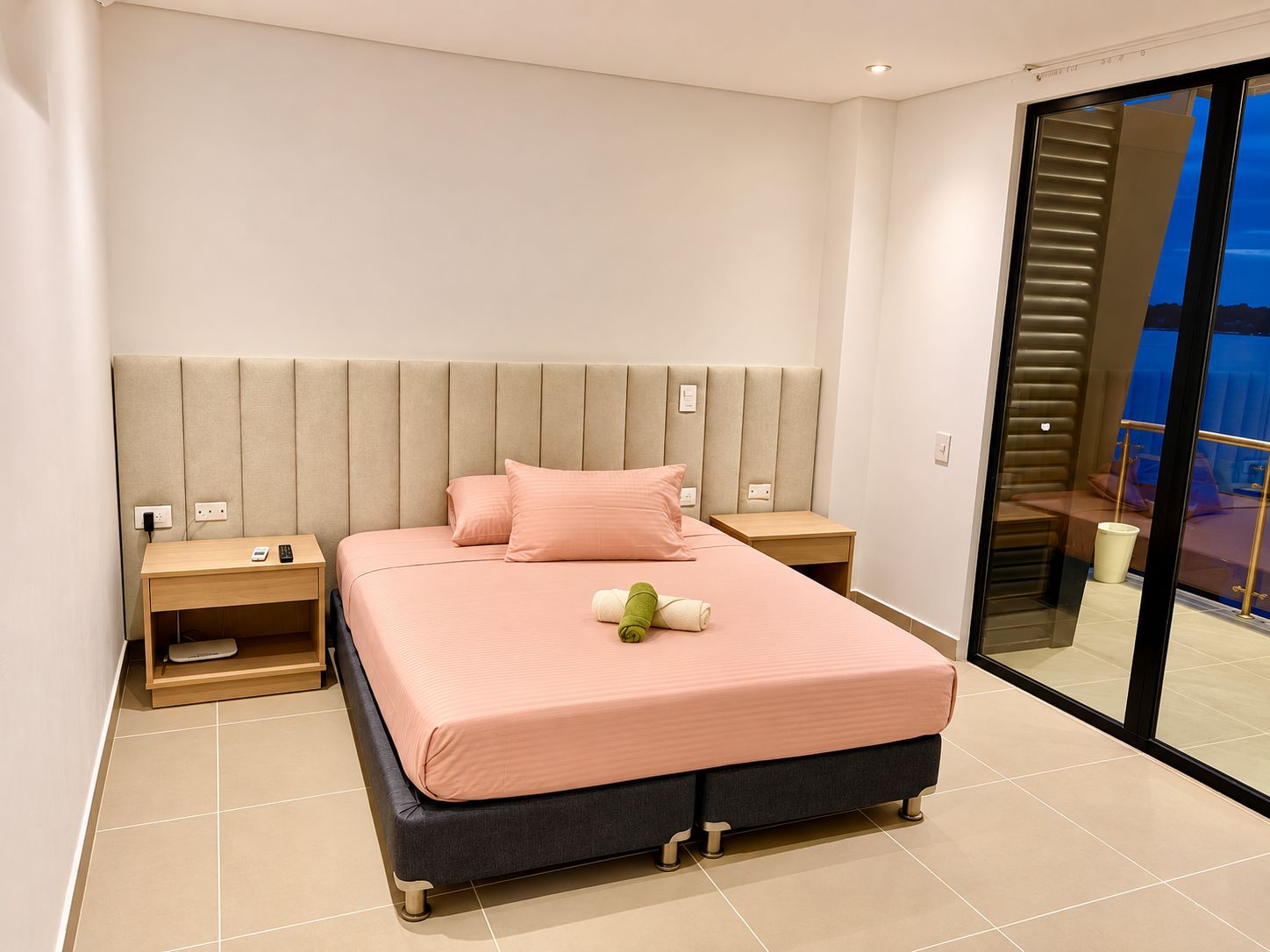 A modern bedroom with a large bed, two bedside tables, and a sliding glass door leading to a balcony.
