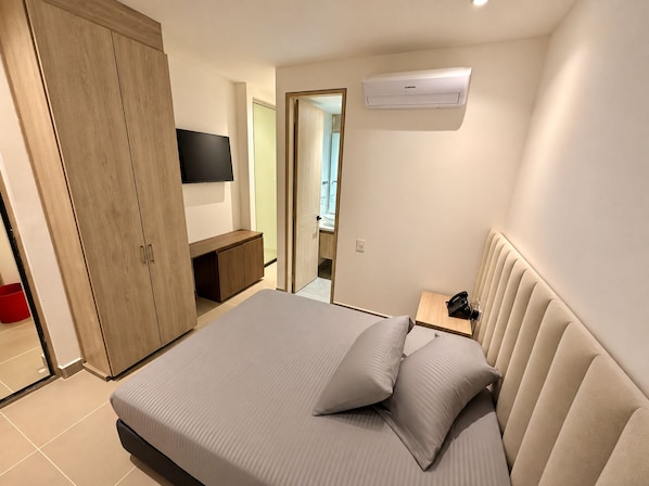 Un dormitorio con cama, armario, televisor y aire acondicionado.