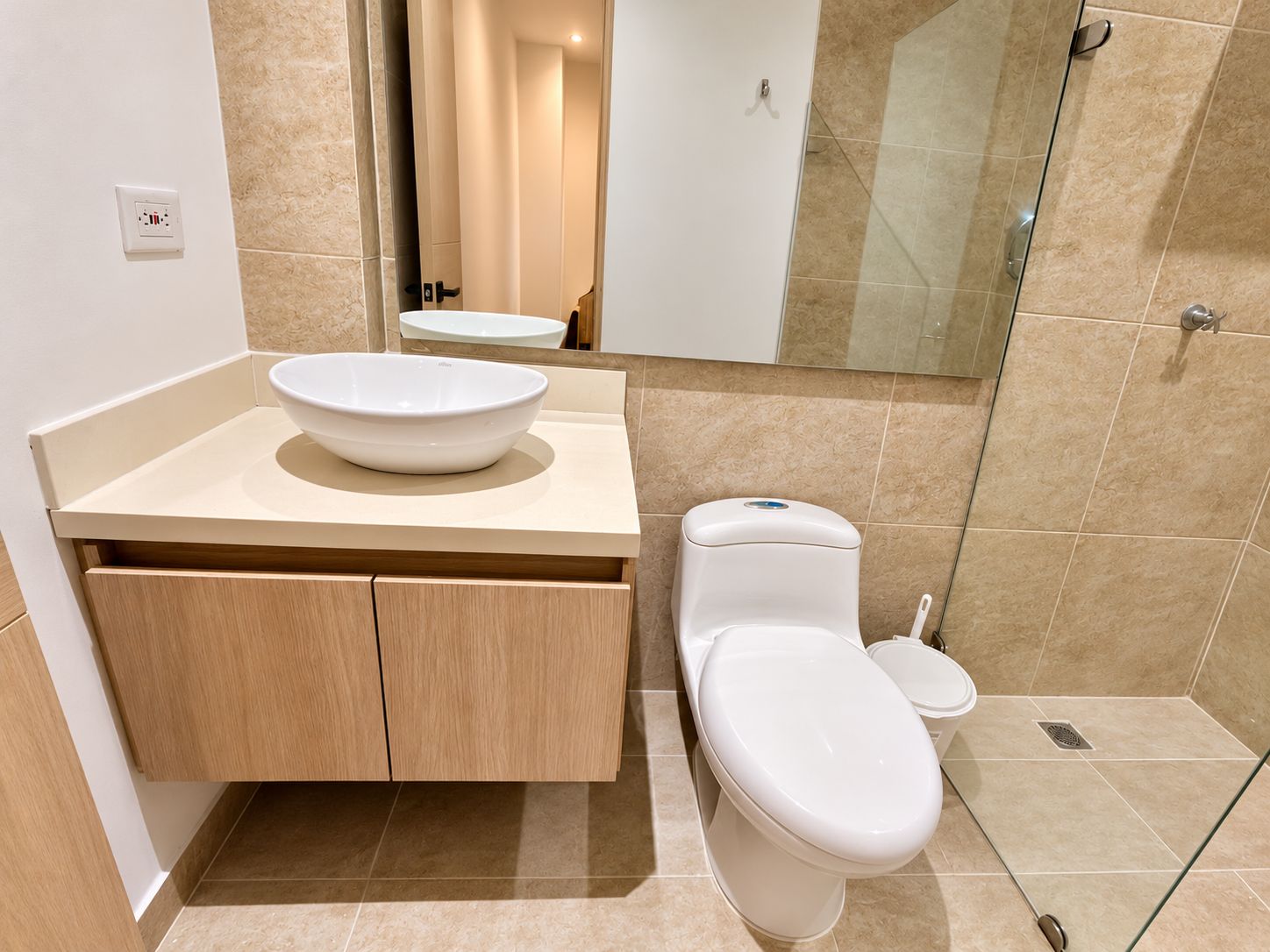 Une salle de bain moderne avec un meuble-lavabo beige, un lavabo blanc en forme de cuvette, des toilettes et une douche à parois de verre.