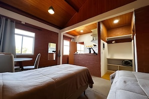 Une chambre avec deux lits, une table à manger et un coin cuisine visible à travers une porte ouverte.