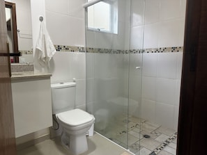A bathroom with a toilet, a glass-enclosed shower, and a window. - Suítes Saint Louis (Campos do Jordão)