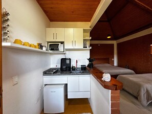 Une petite cuisine équipée d’un four à micro-ondes, d’un petit réfrigérateur et d’un évier. On y trouve deux lits avec une tête de lit en bois, ainsi qu’une petite table avec une bouilloire et des tasses.