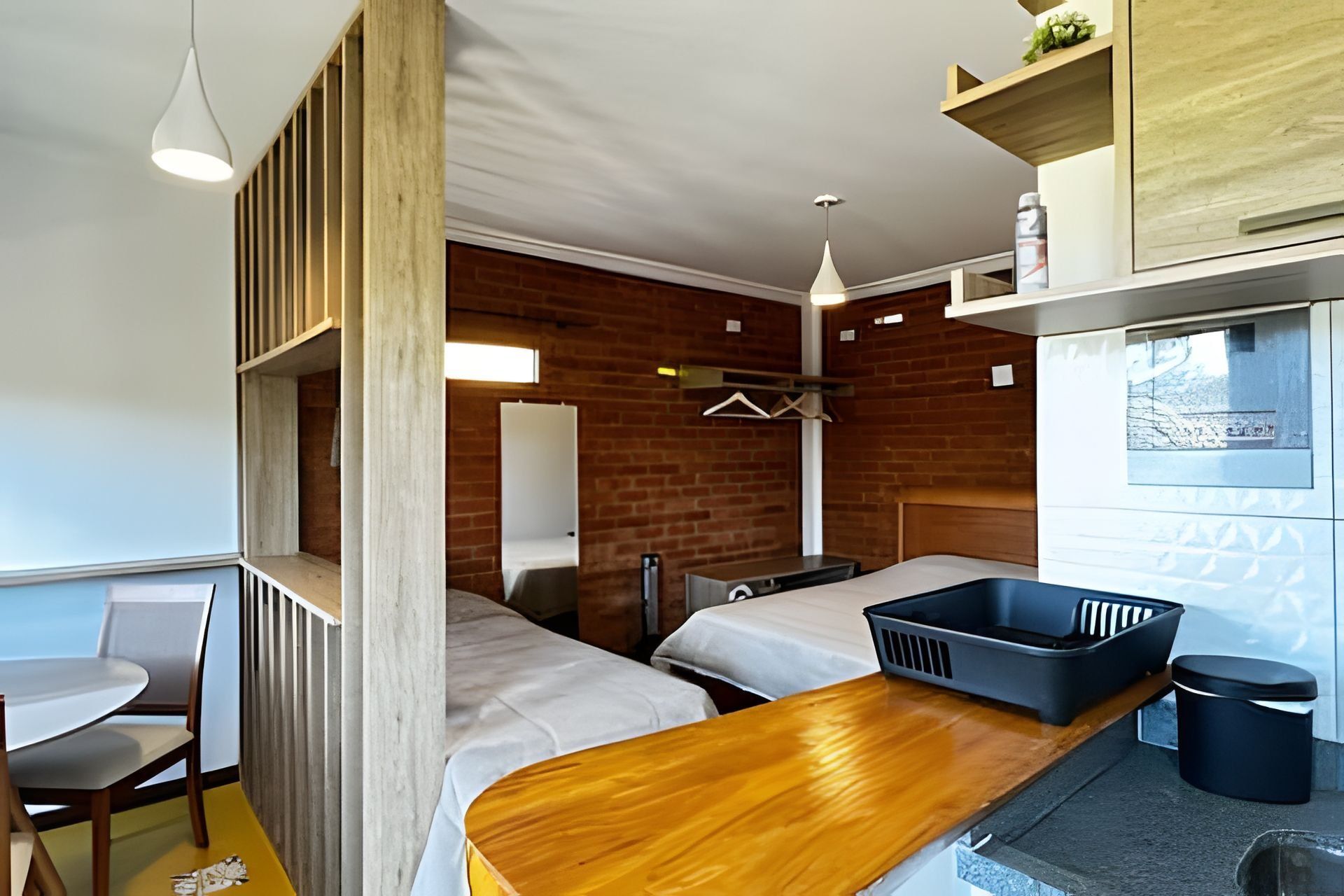 A compact room with a wooden bench, two beds, a small table, and a window with a view.