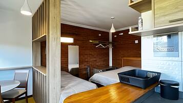 A compact room with a wooden bench, two beds, a small table, and a window with a view.