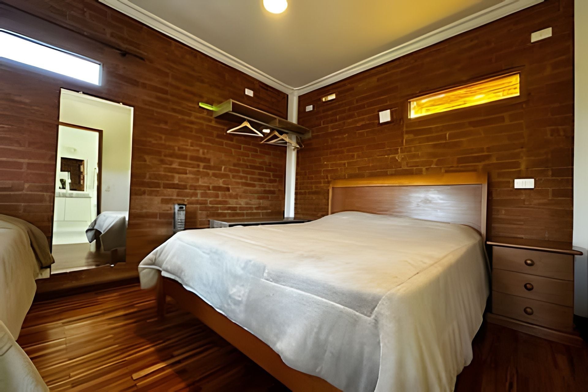 A bedroom with a wooden headboard, a bed with a white bedspread, a wooden dresser, and a mirror on the wall.