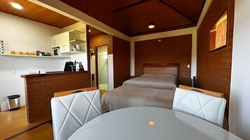 Quarto de hotel compacto com cama, uma mesa pequena e uma kitchenette.