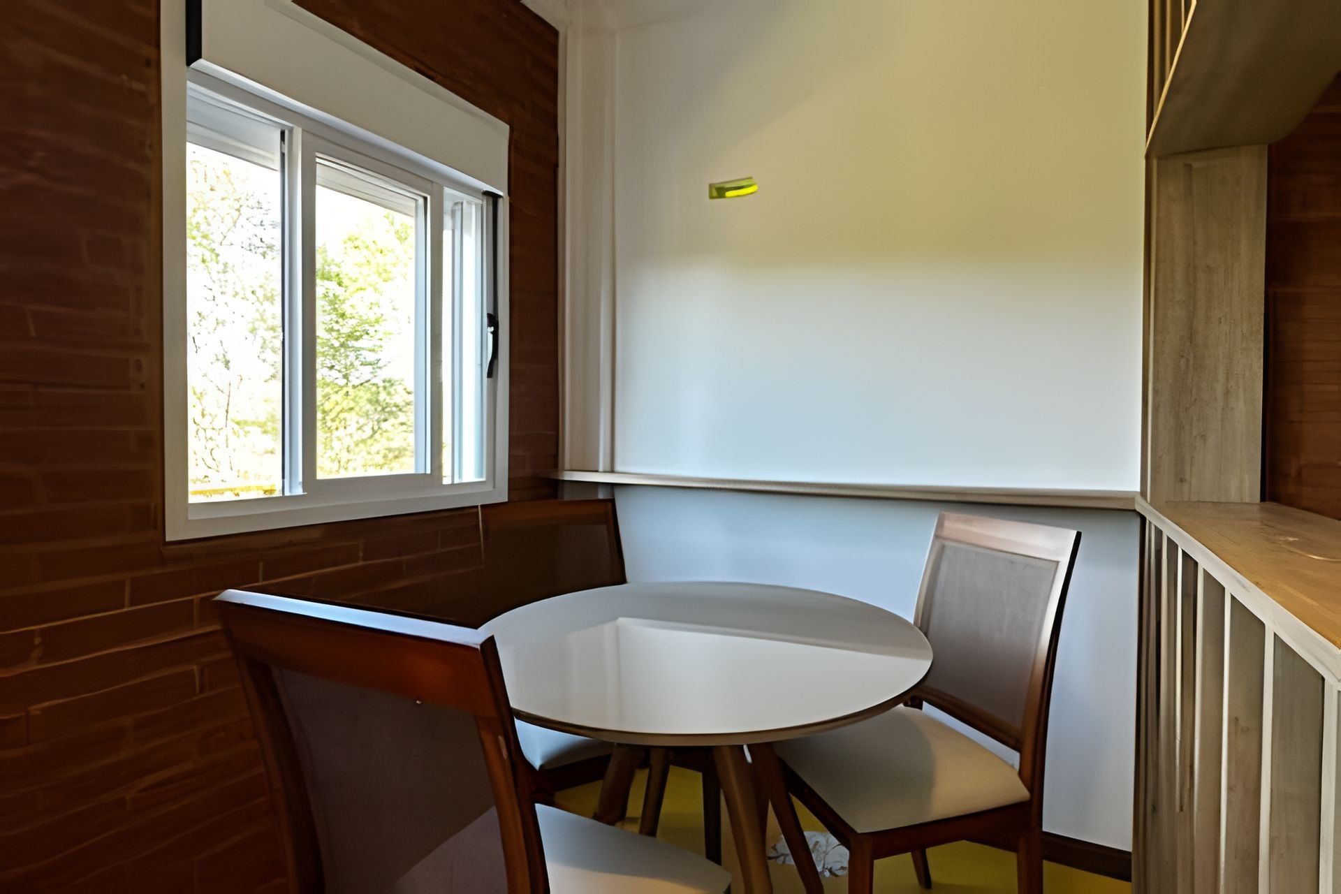 A room with a round table and two chairs, a whiteboard on the wall, and a window with a view of trees.