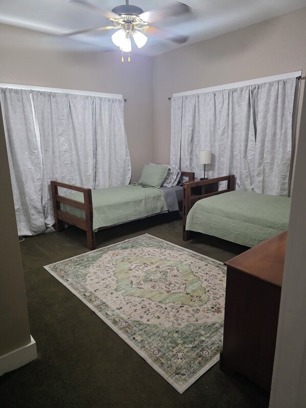 A bedroom with two single beds, a ceiling fan, and a patterned rug.