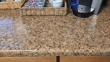 Een aanrecht met een koffiezetapparaat, een mandje koffiekapsules, een mok en een rieten mand met diverse spullen.