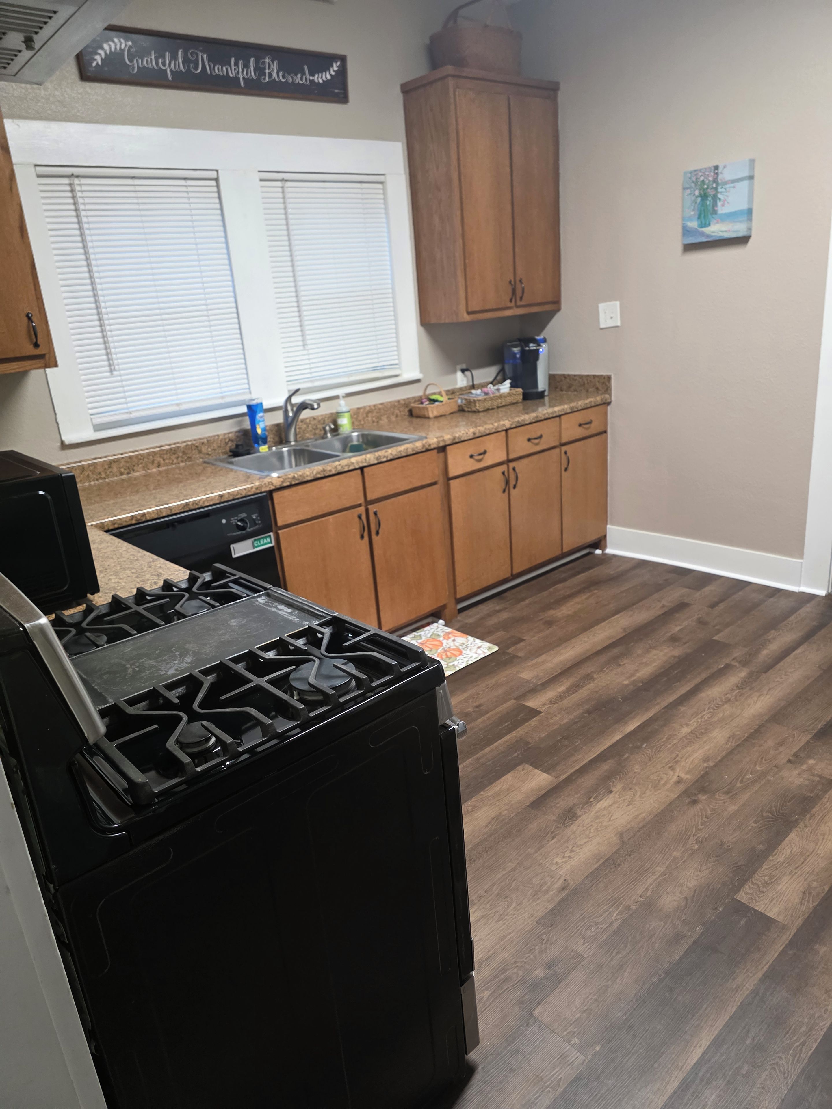 A kitchen with a stove, sink, cabinets, and a window with blinds.