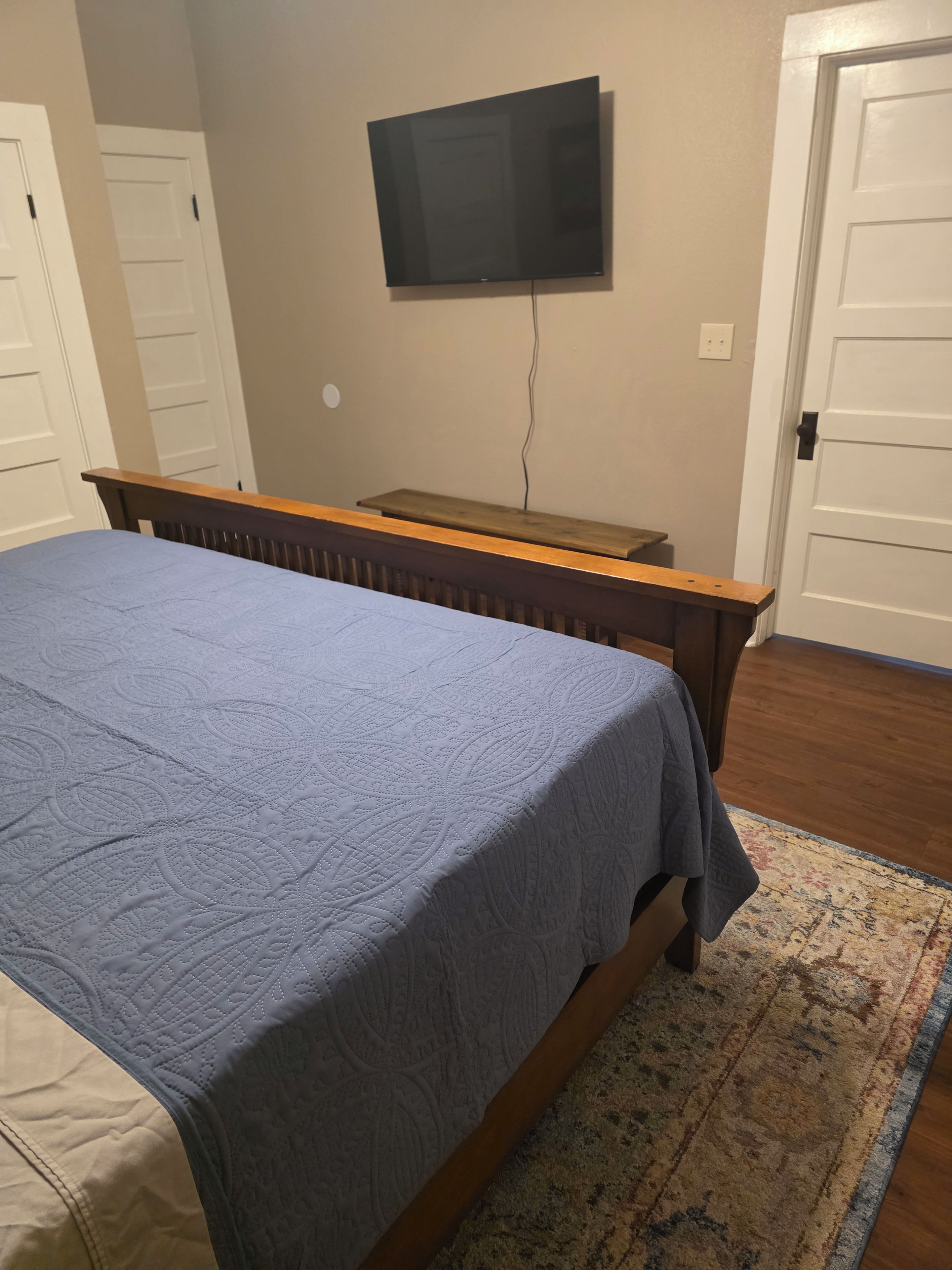 Een slaapkamer met een bed, een aan de muur bevestigde televisie en een houten hoofdeinde.