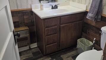 A bathroom with a wooden vanity, a white sink, a toilet, and a green trash bin.