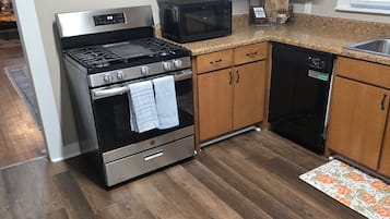 Een keuken met een roestvrijstalen fornuis, een magnetron, houten keukenkastjes en een vaatwasser.