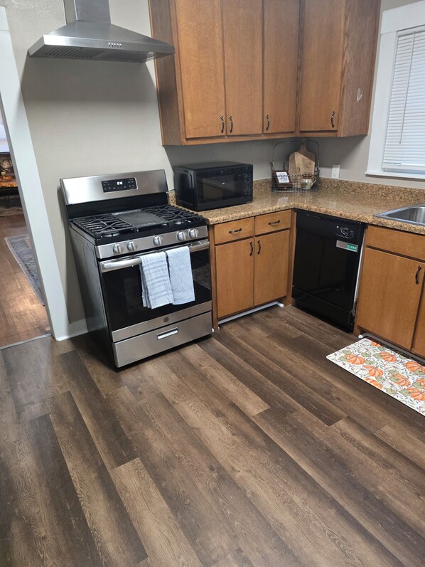 A kitchen with a stainless steel stove, a microwave, wooden cabinets, and a dishwasher. - The Shaded Pecan Cottage (Terrell)