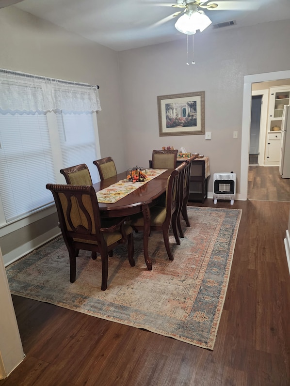A dining area with a wooden table, six chairs, a patterned rug, a ceiling fan, and a framed picture on the wall. - The Shaded Pecan Cottage (Terrell)