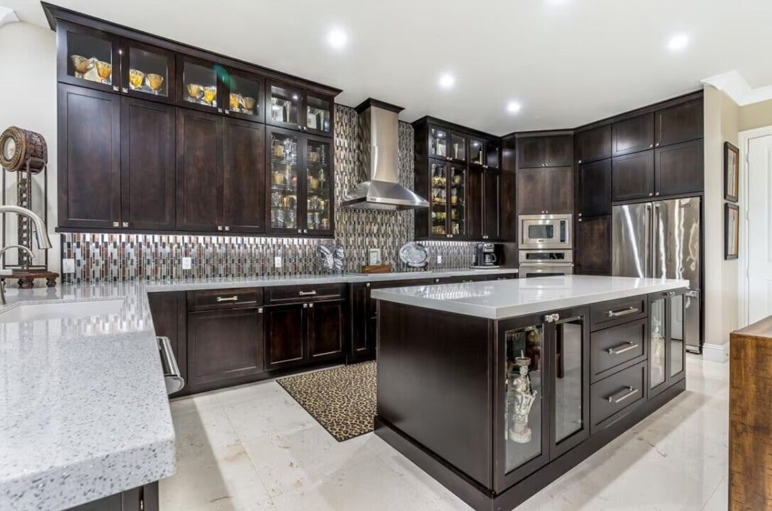 A modern kitchen with dark cabinetry, a central island, stainless steel appliances, and a patterned backsplash.