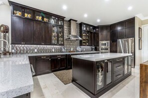 A modern kitchen with dark cabinetry, a central island, stainless steel appliances, and a patterned backsplash. - Sunny Daze~Private Pool Home, 45ft of Dockage, minutes from the beach! (Marathon)