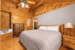 Ein Schlafzimmer mit Holzwandverkleidung, einem Bett, einem Schminktisch, einem Nachttisch und einem Deckenventilator.