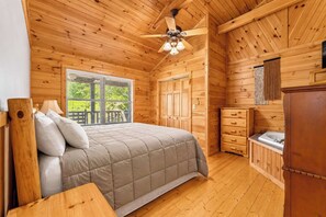 A wooden cabin bedroom with a bed, a ceiling fan, a window with blinds, and a wooden dresser. - Stonebridge Retreat | Hot Tub • Near Everything! (Sevierville)