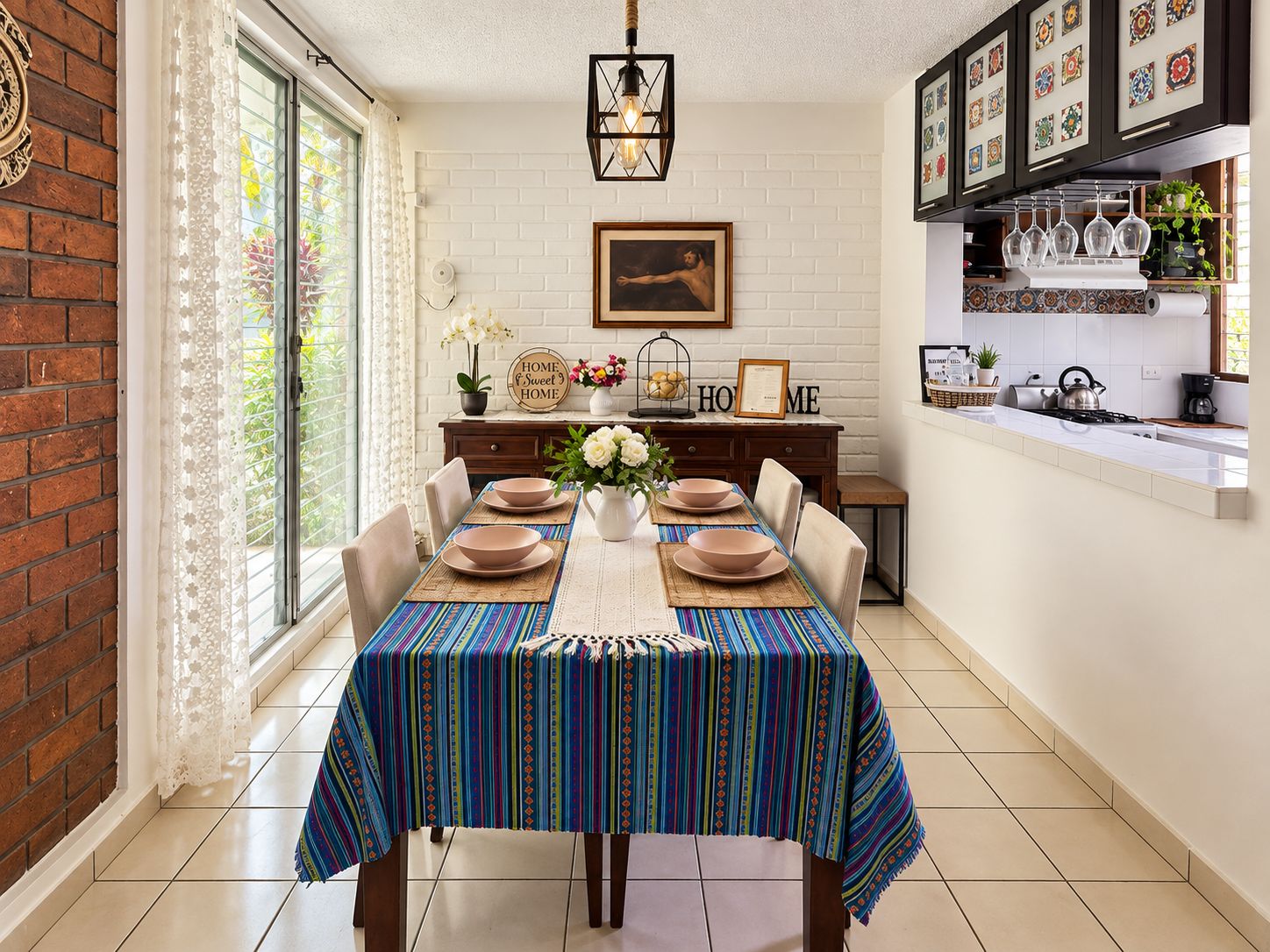 Un coin repas avec une table dressée pour quatre personnes, un mur en briques et un espace cuisine équipé d’une cuisinière et d’étagères.
