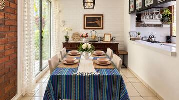 Un coin repas avec une table dressée pour quatre personnes, un mur en briques et un espace cuisine équipé d’une cuisinière et d’étagères.