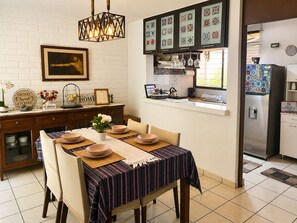 A kitchen with a dining table set for four, a refrigerator, and a window with decorative tiles. - La Casa del Pasaje (San Salvador)