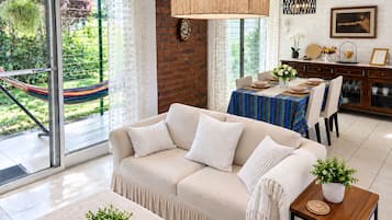 Un salon moderne avec un canapé, une table à manger et une vue sur un jardin grâce à de grandes fenêtres.