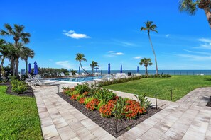 A pool area with lounge chairs and umbrellas, surrounded by palm trees and a clear sky. - Beachfront Escape in the Moorings | Gulf Views & Coastal Breeze (Naples)