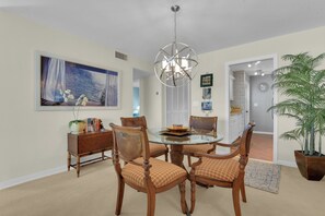 A dining area with a glass table surrounded by wooden chairs, a chandelier, and a painting on the wall. - Beachfront Escape in the Moorings | Gulf Views & Coastal Breeze (Naples)
